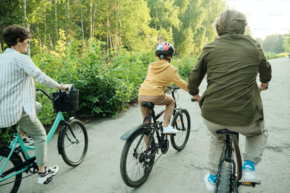 Active family of husband, wife and their son of elementary age riding bicycles along road in modern park on sunny day or morning