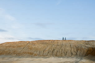 Pequeñas siluetas de dos investigadores contemporáneos con overoles protectores que se mueven en la cima de una colina larga contra un cielo azul claro