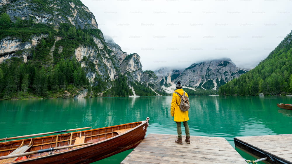 Vue arrière d’un randonneur avec les bras tendus visitant le lac alpin à Braies, en Italie. Randonneur heureux vêtu d’une veste jaune et d’un sac à dos profite du paysage naturel à l’automne. Envie de voyager et de voyager.
