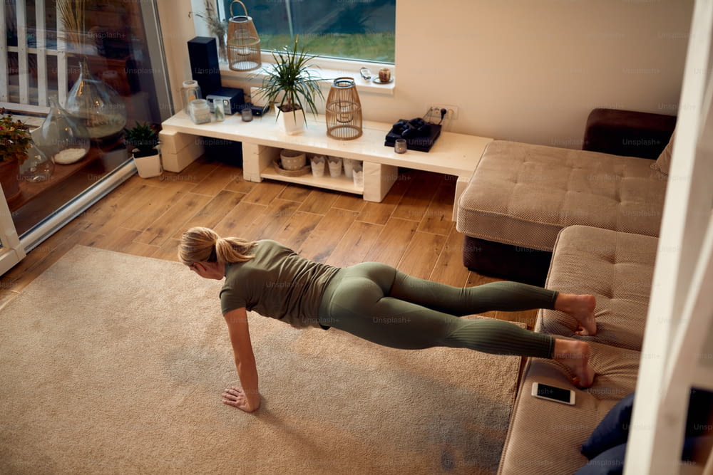High angle view of sportswoman doing push-ups while holding her legs on the sofa during home workout.