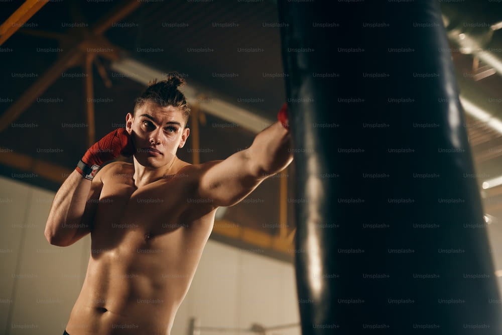 Niedriger Winkelblick auf junge Kämpfer, die Boxsack während des Sporttrainings in einem Fitnessstudio boxen.