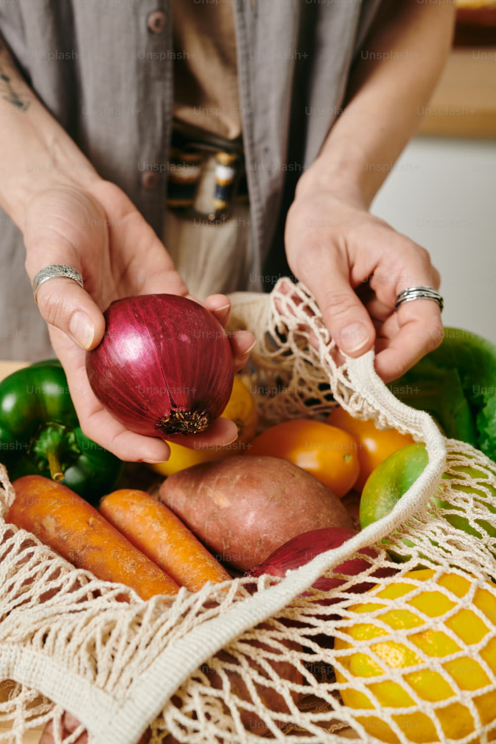 Female vegetarian holding fresh onion over bag with other vegetables