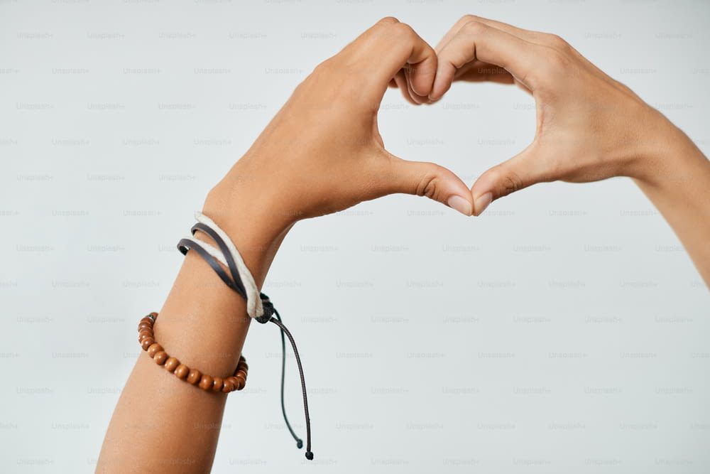 Close-up of gay women making heart shape of their hand against white background.