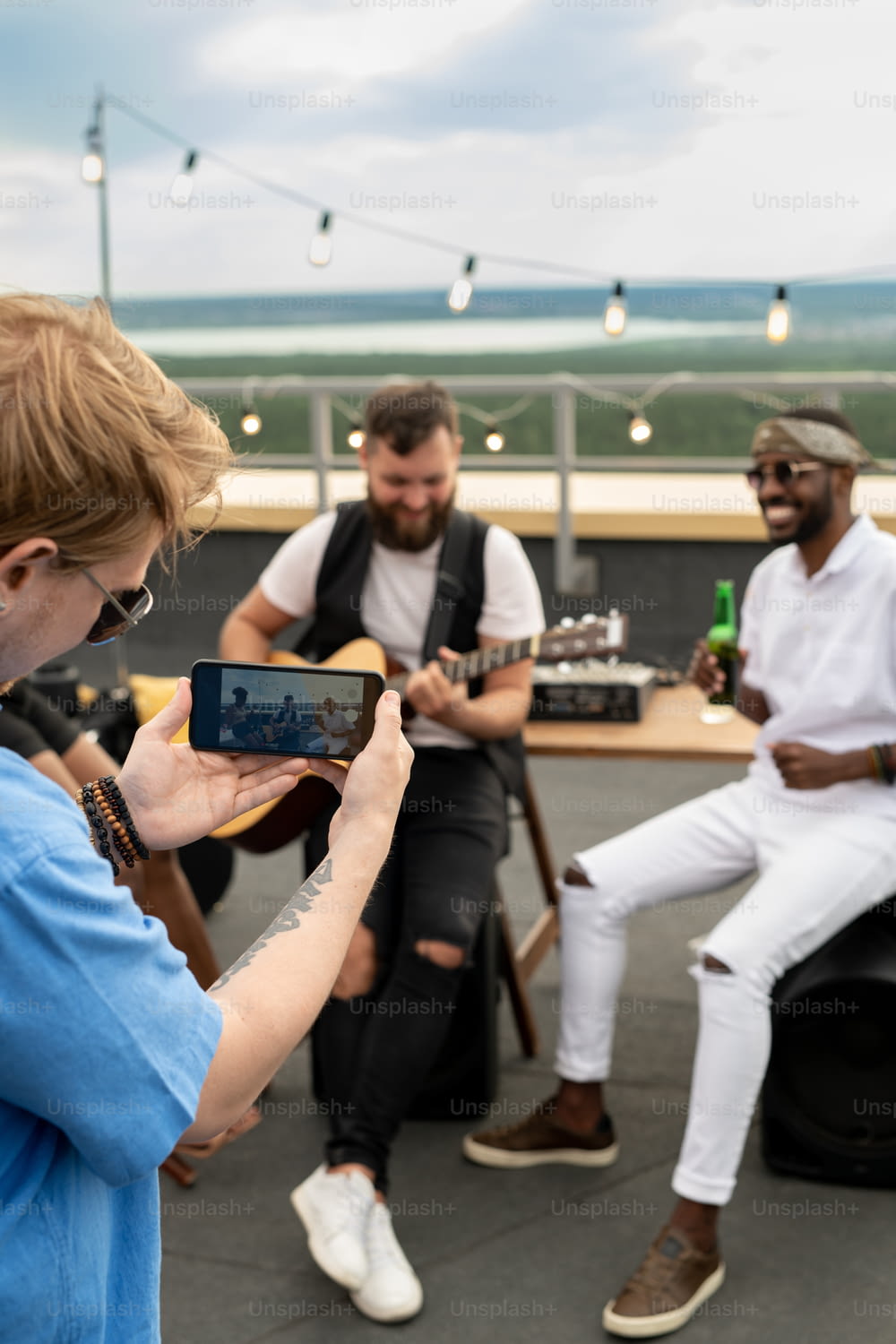 Young man shooting video on smartphone of his happy friends enjoying rooftop party