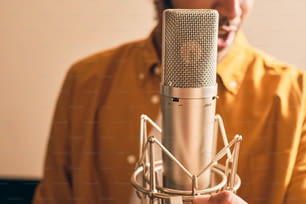 Nahaufnahme eines marokkanischen Mannes im gelben Hemd singt mit Mikrofon im professionellen Aufnahmestudio