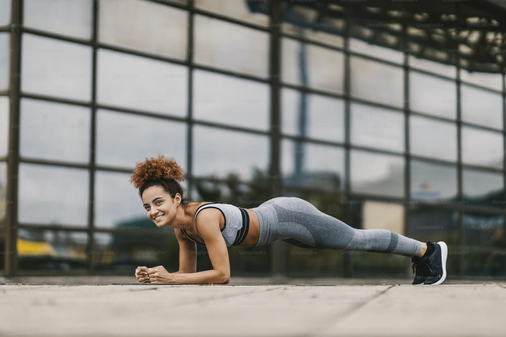 Young happy, fit sportswoman doing planks near the building in an urban district. Hard work, healthy lifestyle is a key to a good and happy life