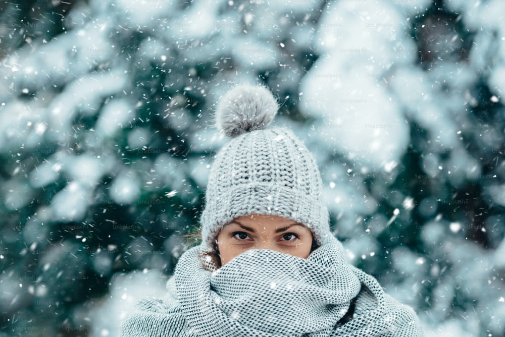 눈이 내리는 추운 겨울날에 스카프와 모자를 쓴 아름다운 젊은 여성의 초상화