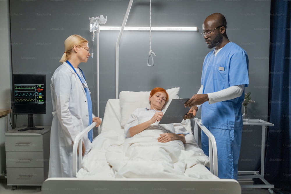 Femme âgée signant un accord d’opération donné par l’anesthésiste et le médecin debout près du lit dans le service hospitalier