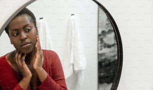 Reflection in mirror of Black African woman touching and inspecting her face. Self care and skin care