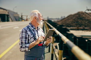建設現場での作業の管理。高齢作業員がタブレットを片手に高速道路に立ち、作業状況を確認しています。