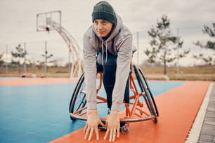 Jovem jogador de basquete em cadeira de rodas fazendo exercícios de alongamento em quadra ao ar livre antes do treinamento esportivo.