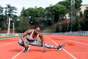 Stockfoto einer afroamerikanischen Sprinterin, die ihre Beine vor dem Training ausstreckt