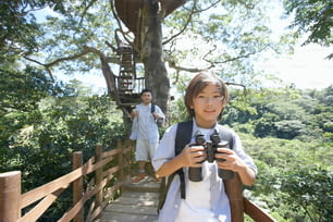a young boy holding a camera while standing on a bridge