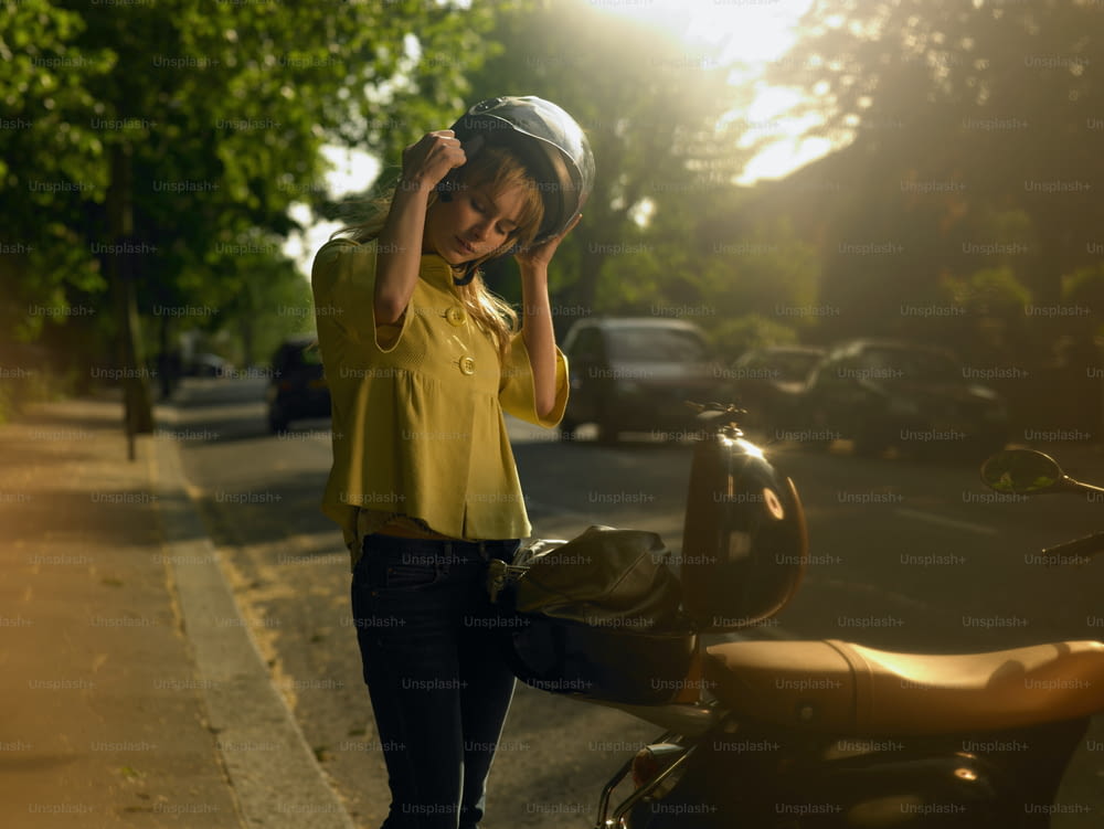 Una mujer con una camisa amarilla está parada junto a una motocicleta