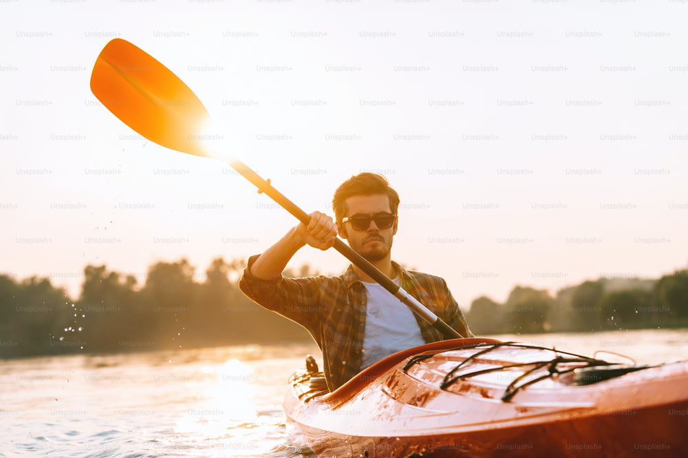 Handsome young man kayaking on river with sunset in the background