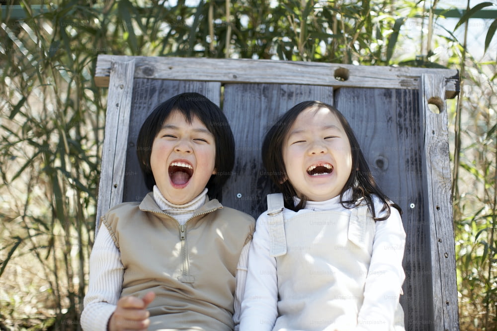 two young girls sitting on a wooden bench with their mouths open