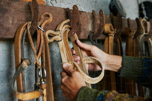 Una persona sosteniendo un par de tijeras frente a una pared de tachuelas de caballo