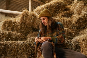 Un hombre sentado en una pila de heno mirando su teléfono celular