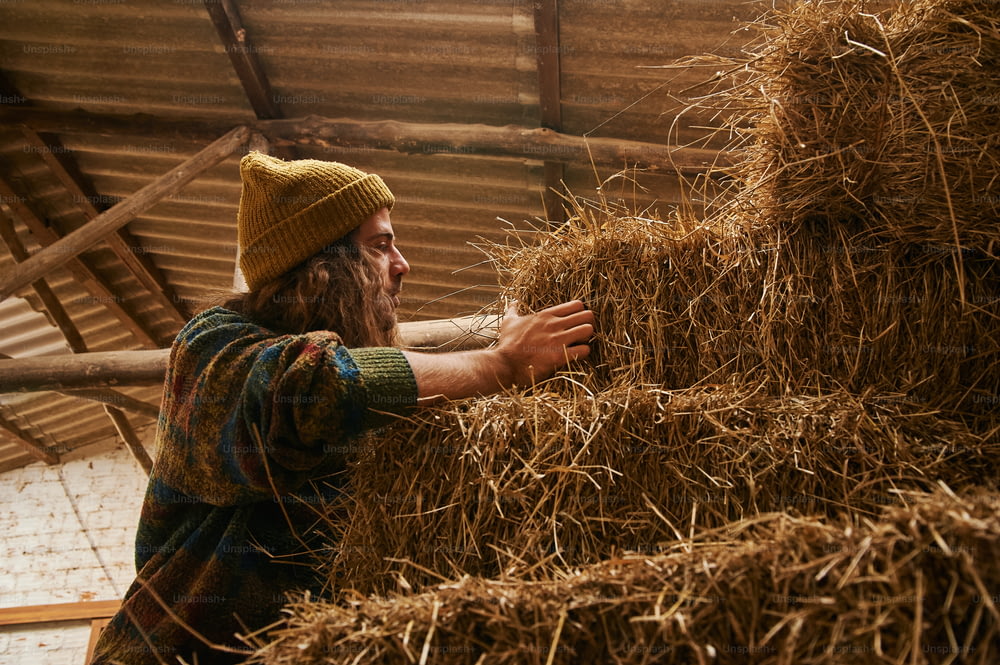 a man with long hair and a beard is holding a bale of hay