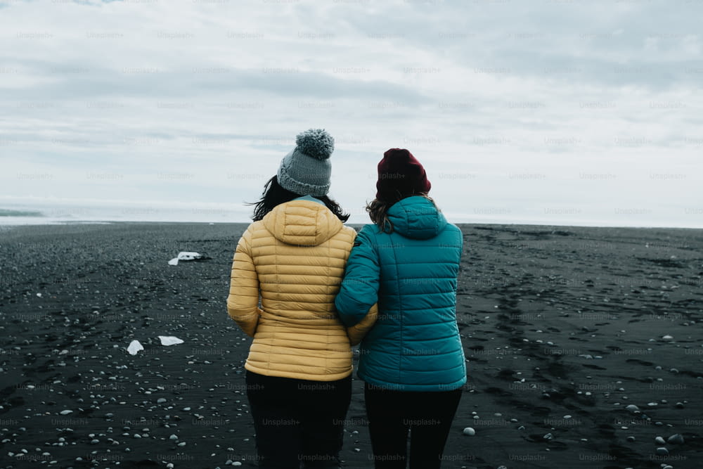 Duas mulheres em pé em uma praia olhando para o oceano