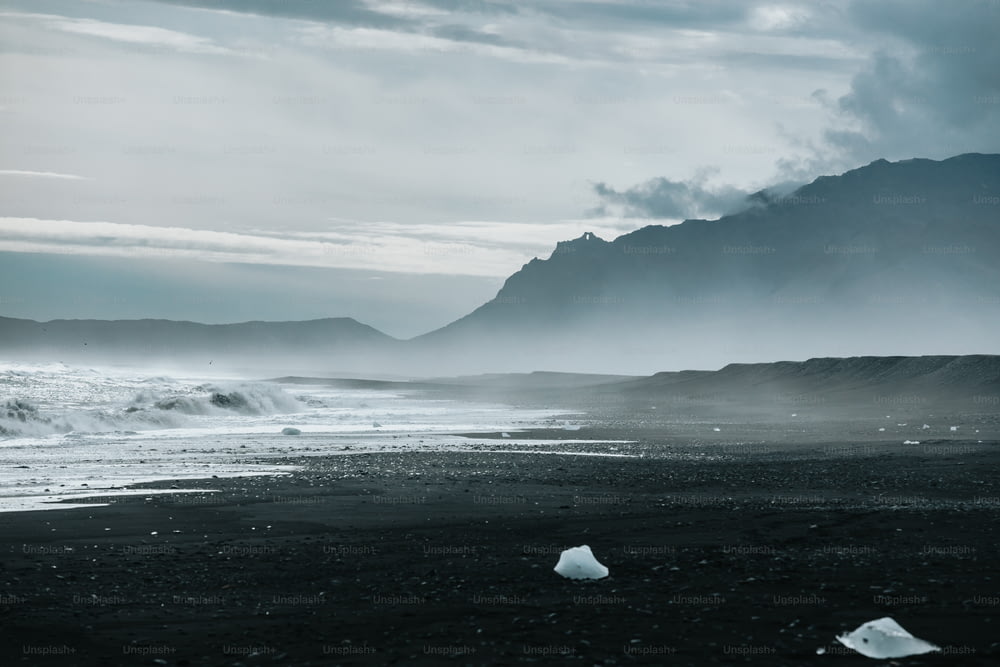 Una foto en blanco y negro de una playa con montañas al fondo