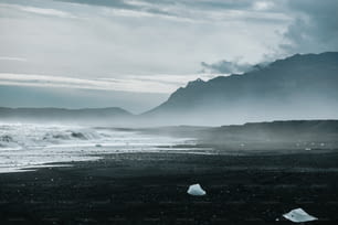uma foto em preto e branco de uma praia com montanhas ao fundo
