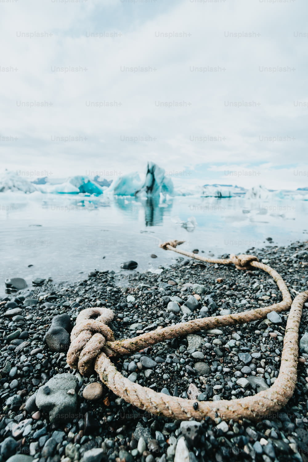 a rope on a rocky beach with icebergs in the background