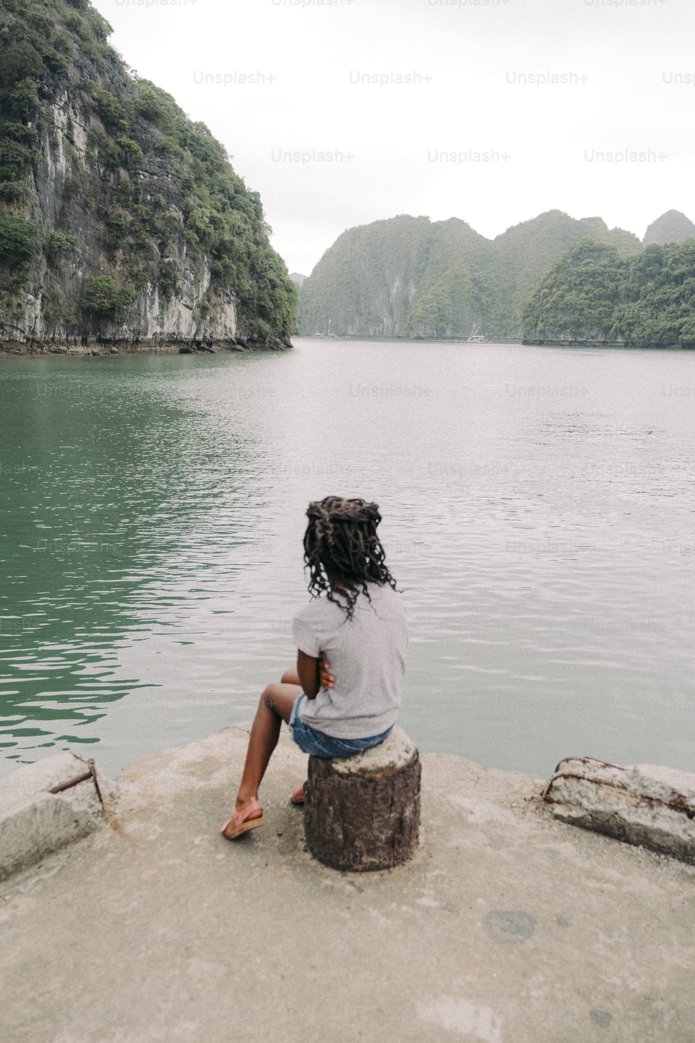 uma pessoa sentada em uma rocha perto de um corpo de água