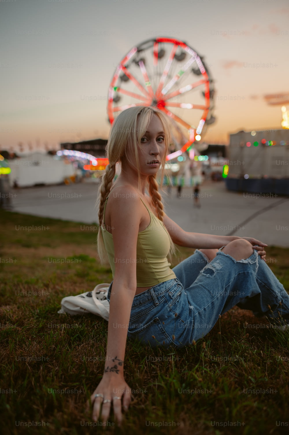 a woman sitting in the grass with a ferris wheel in the background