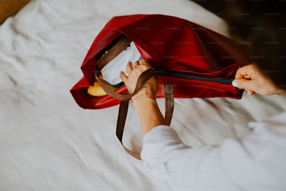 a person holding a red bag on top of a bed