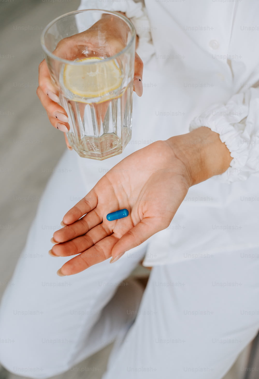 uma mulher segurando um copo de água e uma pílula azul