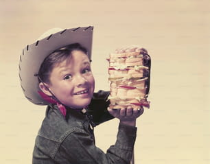 Ein kleiner Junge, der einen Cowboyhut trägt und ein Sandwich hält