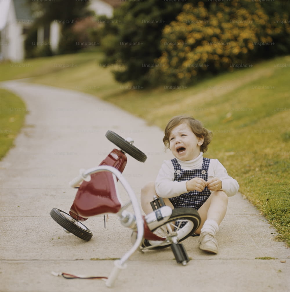 Una bambina seduta a terra accanto a una bici rossa