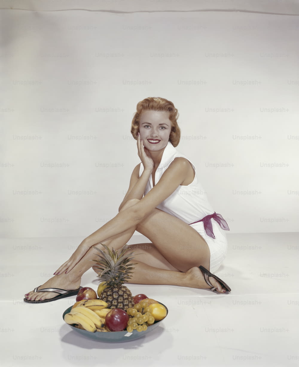 Eine Frau, die neben einem Teller mit Obst auf dem Boden sitzt