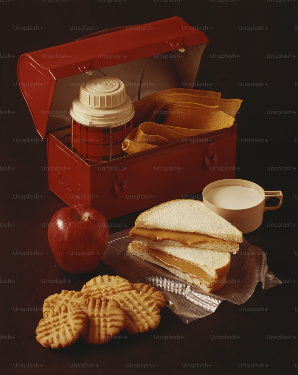 a lunch box with a sandwich, crackers and an apple