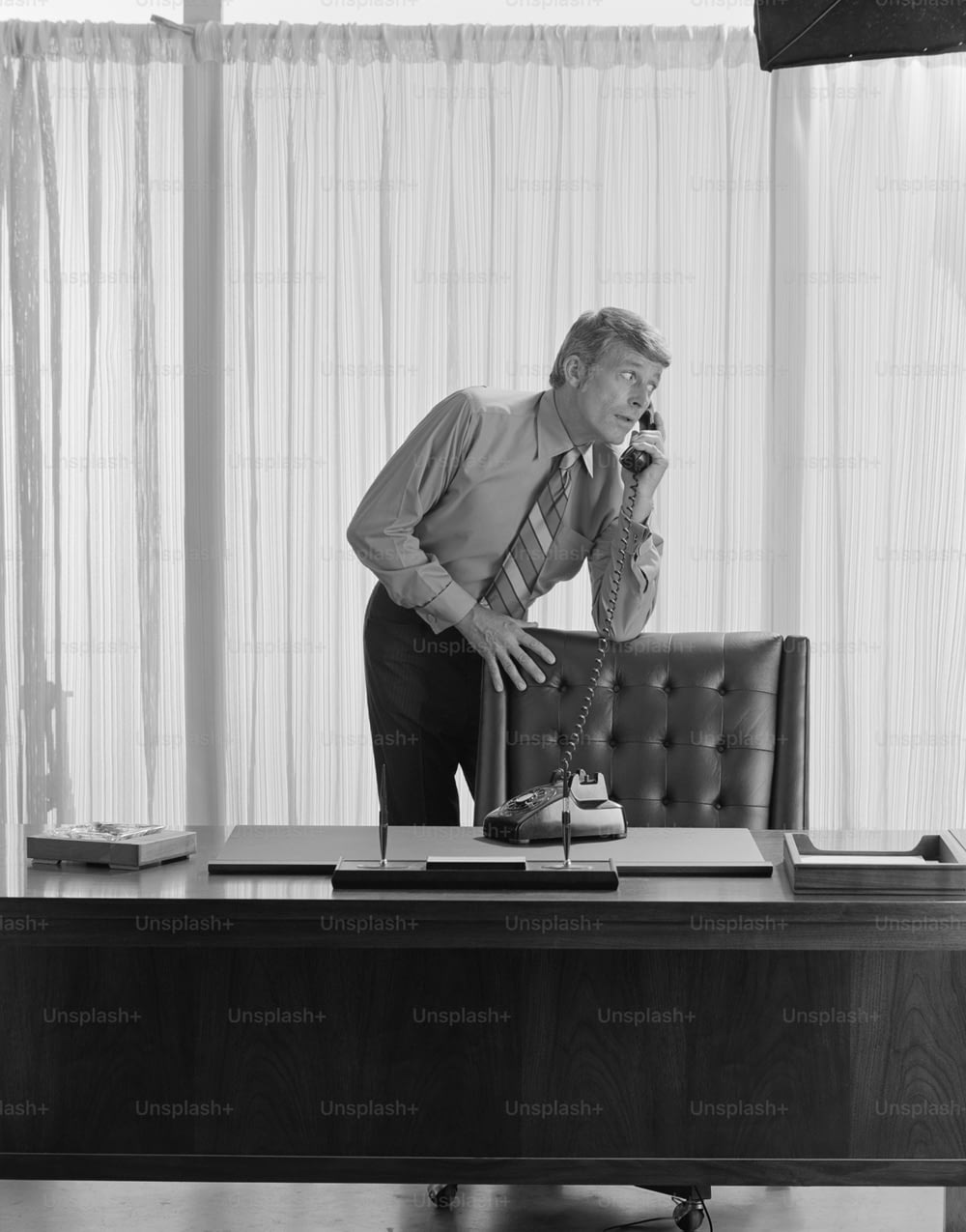 a man standing at a desk talking on a phone