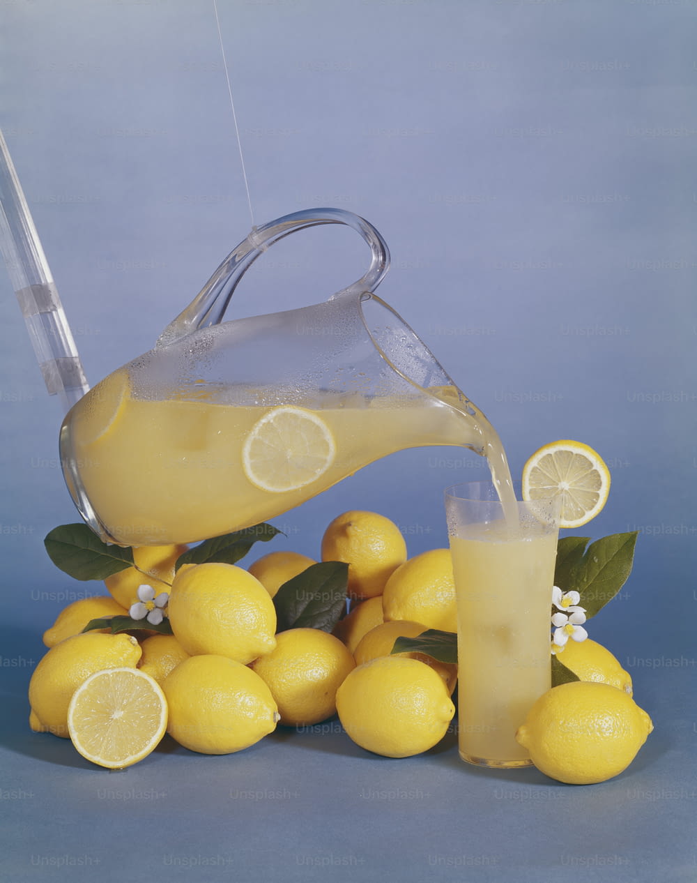 a pitcher of lemonade being poured over a pile of lemons