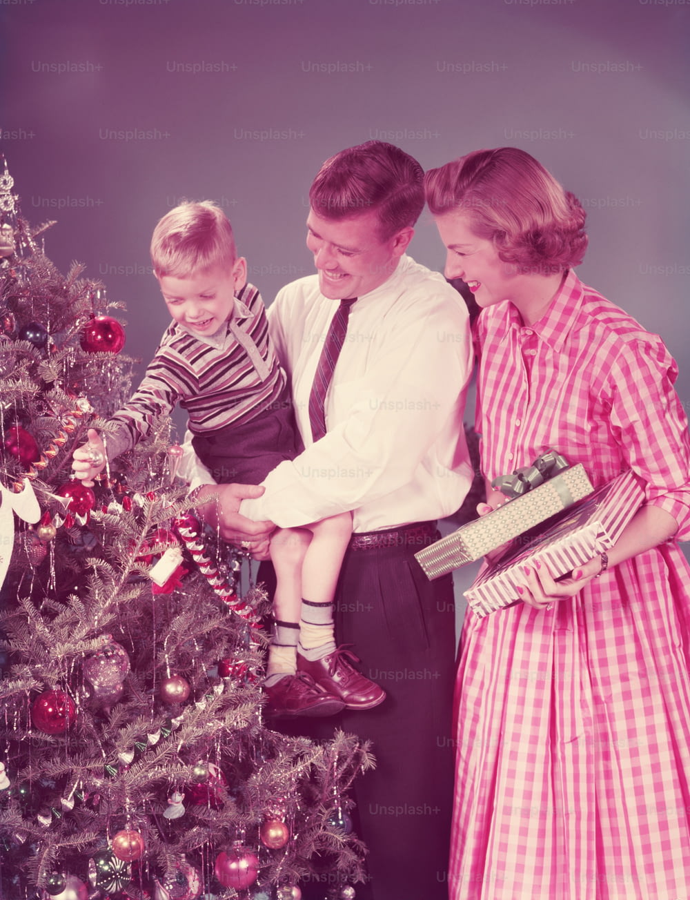 UNITED STATES - CIRCA 1950s:  Family at Christmas, mother holding presents, father carrying son.