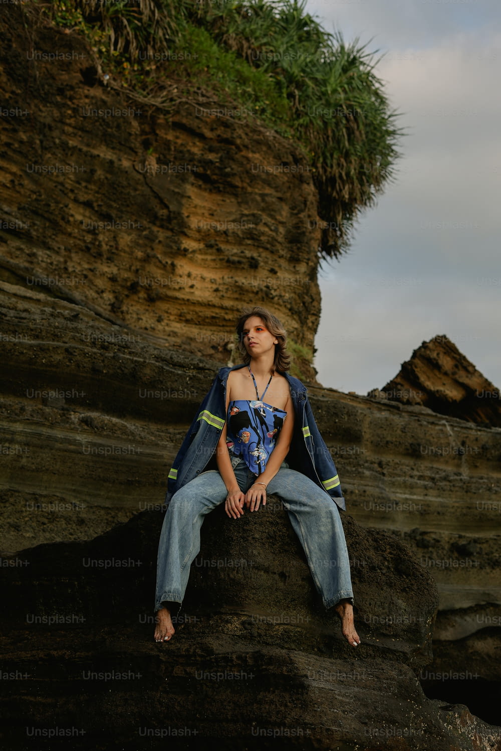 a woman sitting on top of a rock next to a cliff