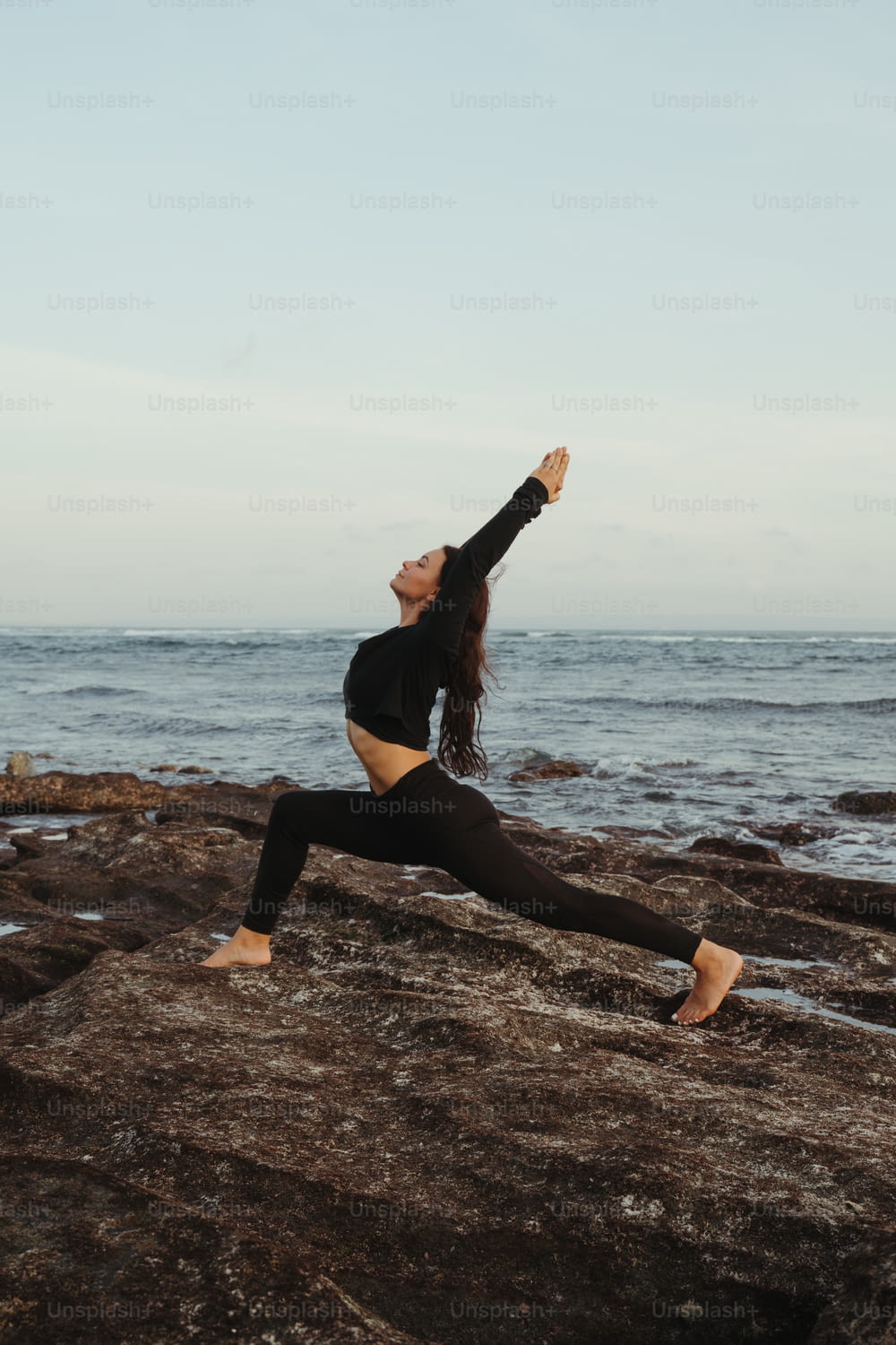 a woman doing a yoga pose on a rock by the ocean