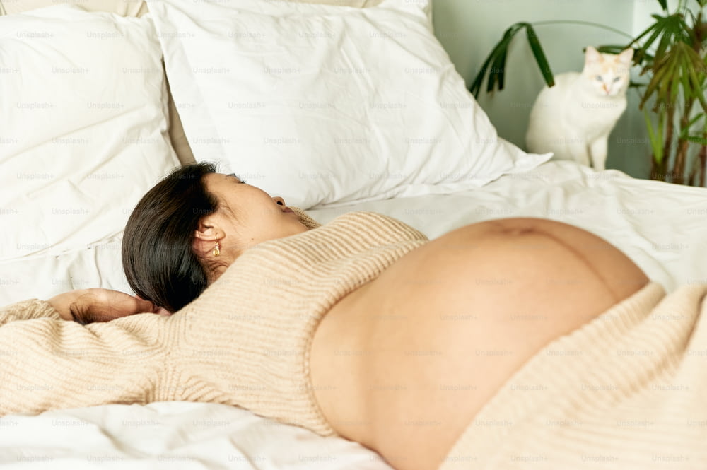 Una mujer embarazada acostada en una cama con un gato en el fondo