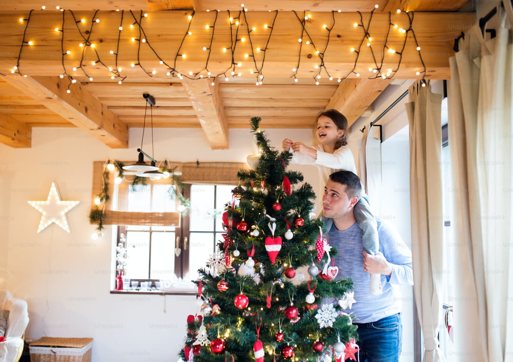 Young father giving his little daughter piggyback decorating Christmas tree together.