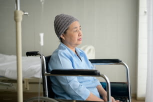 Une patiente asiatique atteinte d’un cancer, déprimée et désespérée, portant un foulard sur la tête à l’hôpital.