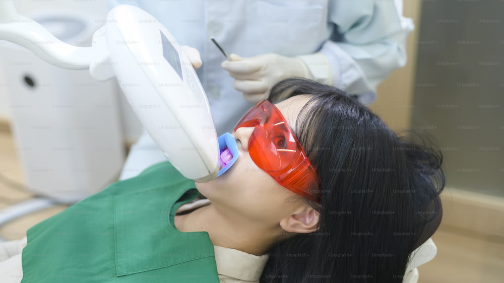 A woman wearing protective glasses  examining by stomatologist , Tooth whitening by ultraviolet lamp