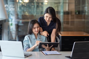 Deux jeunes femmes d’affaires asiatiques sont heureuses de travailler sur des présentations à l’aide de papiers et de tablettes placés au bureau.