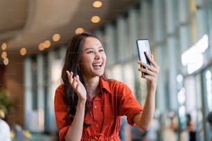 幸せアジアの女性女性の笑顔の手の波は、ビデオ通話スマートフォンデバイスを介して家族にキスをしますぼかしモールの背景で社会的距離の挨拶ニューノーマルライフスタイル