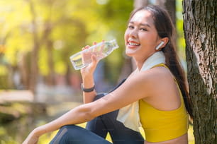 giovane donna che beve acqua dalla bottiglia di acqua potabile femminile asiatica dopo esercizi o sport. Bella donna atleta di fitness che beve acqua pura dopo l'allenamento che si esercita sull'allenamento sportivo mattutino