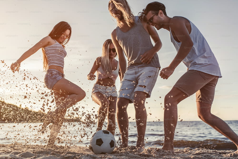 Group of young attractive friends are having fun on beach and playing football