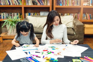 pretty caucasian girl kid enjoy painting crayon color art on paper with mom on sofa background home family concept