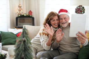 Front view of happy senior couple indoors at home at Christmas, taking selfie.